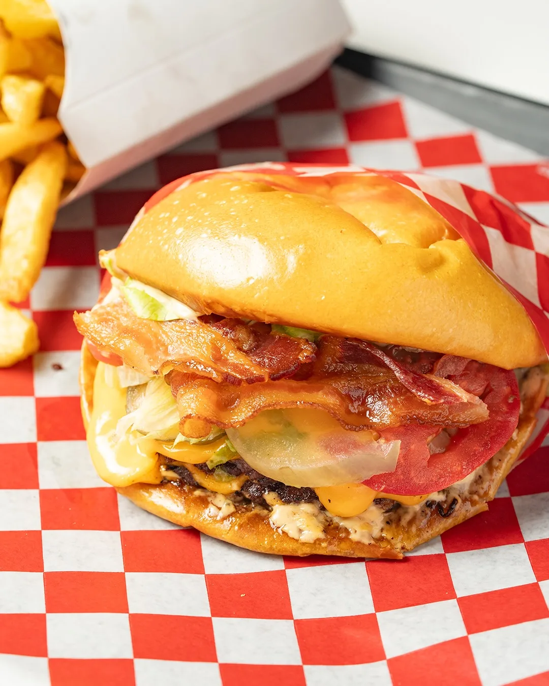 MeatMac Deluxe sobre papel a cuadros, con doble bacon, cheddar, tomate, lechuga y pickle