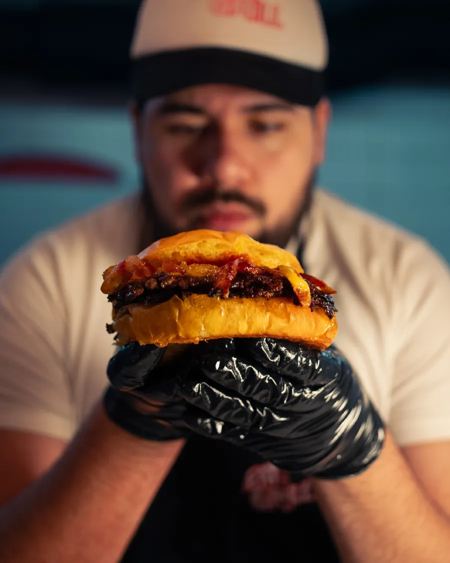 Parrillero sosteniendo una burger con guantes negros