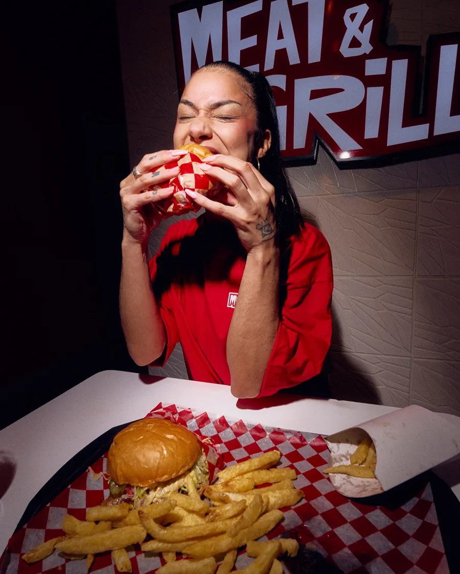 Chica mordiendo una burger bajo el cartel