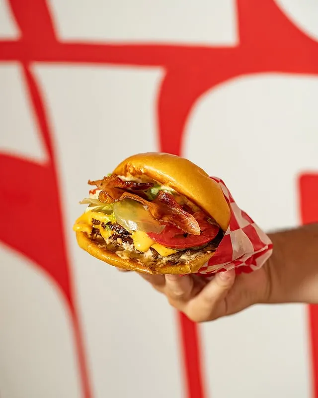Mano sosteniendo una burger frente a la pared roja y blanca