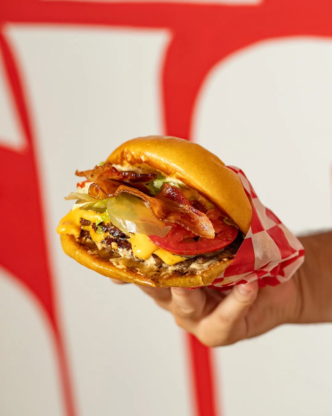 Mano sosteniendo una MeatMac Deluxe con doble bacon y cheddar